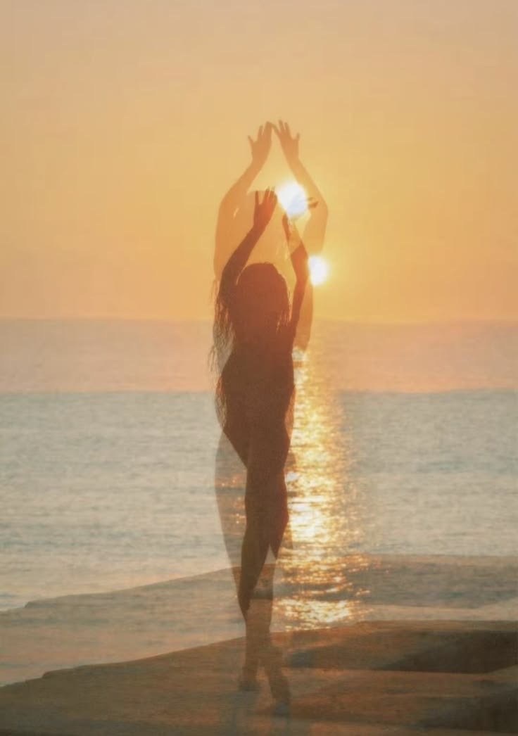 Woman raising her arms to the sun at sunset by the sea