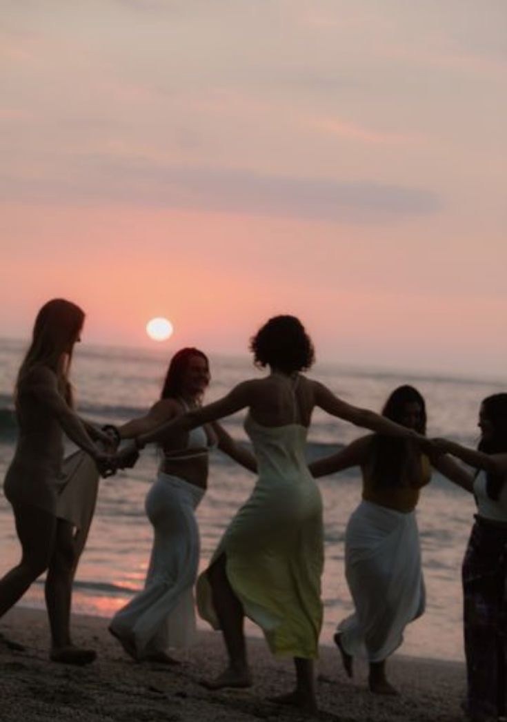 Women dancing hand in hand on the beach at sunset